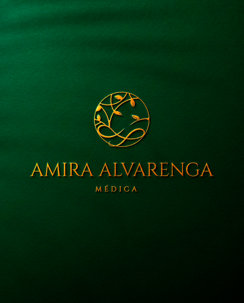 Um logotipo profissional para Amira Alvarenga Médica, desenvolvido pela Agencia azzy - marketing para medicos. O design elegante apresenta um emblema circular dourado texturizado com ramos entrelaçados em um fundo verde esmeralda profundo. Abaixo, o nome 'AMIRA ALVARENGA' está escrito em uma fonte serifada dourada e limpa, com a palavra 'MÉDICA' em uma fonte menor e mais fina por baixo, também em dourado.